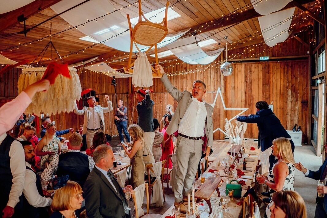 Wedding guests on their feet in a barn venue during a singing waiters show