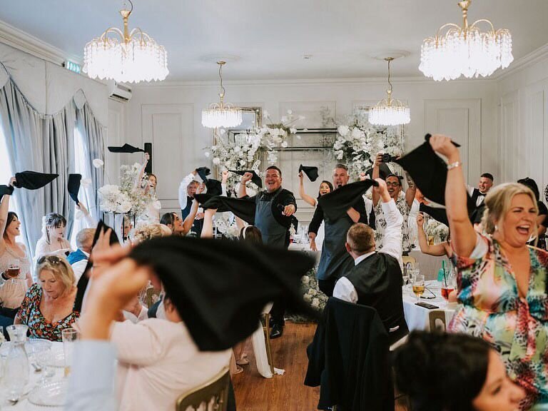 Guests waving napkins in a chandelier-lit wedding venue