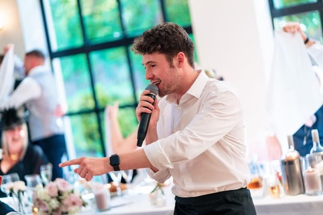 Singing waiter performing to guests beside a window at a wedding