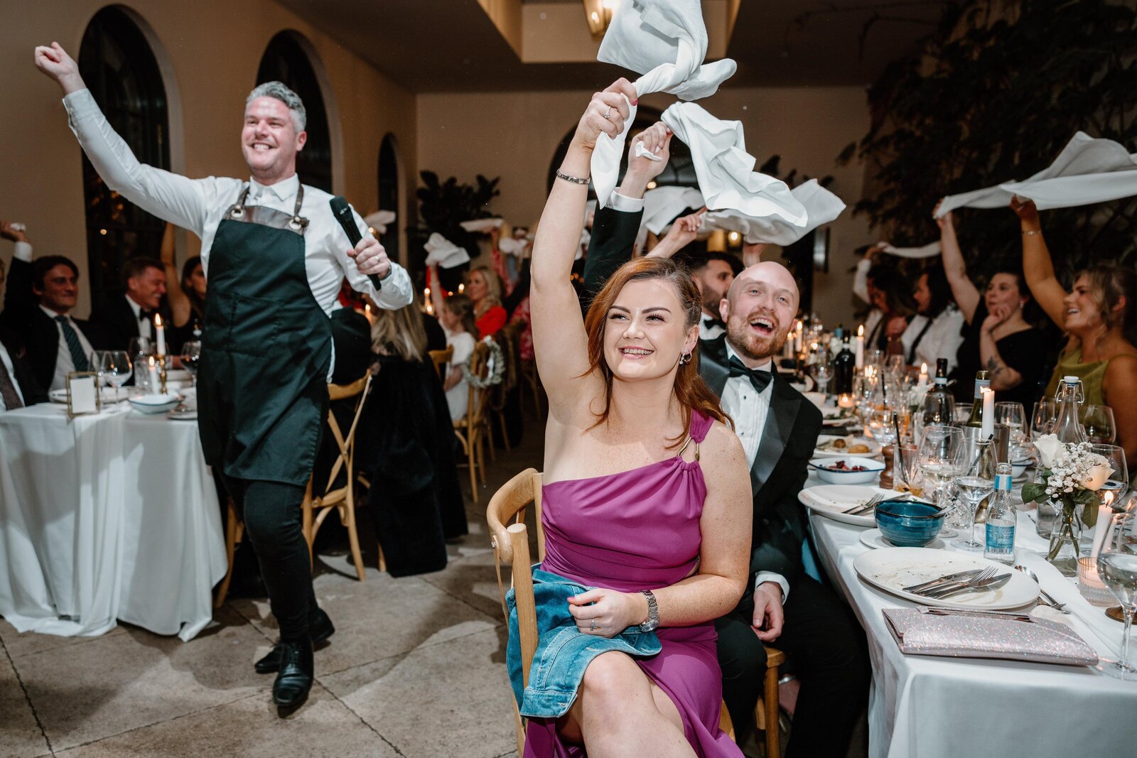 Guests waving napkins as a singing waiter performs at an evening wedding