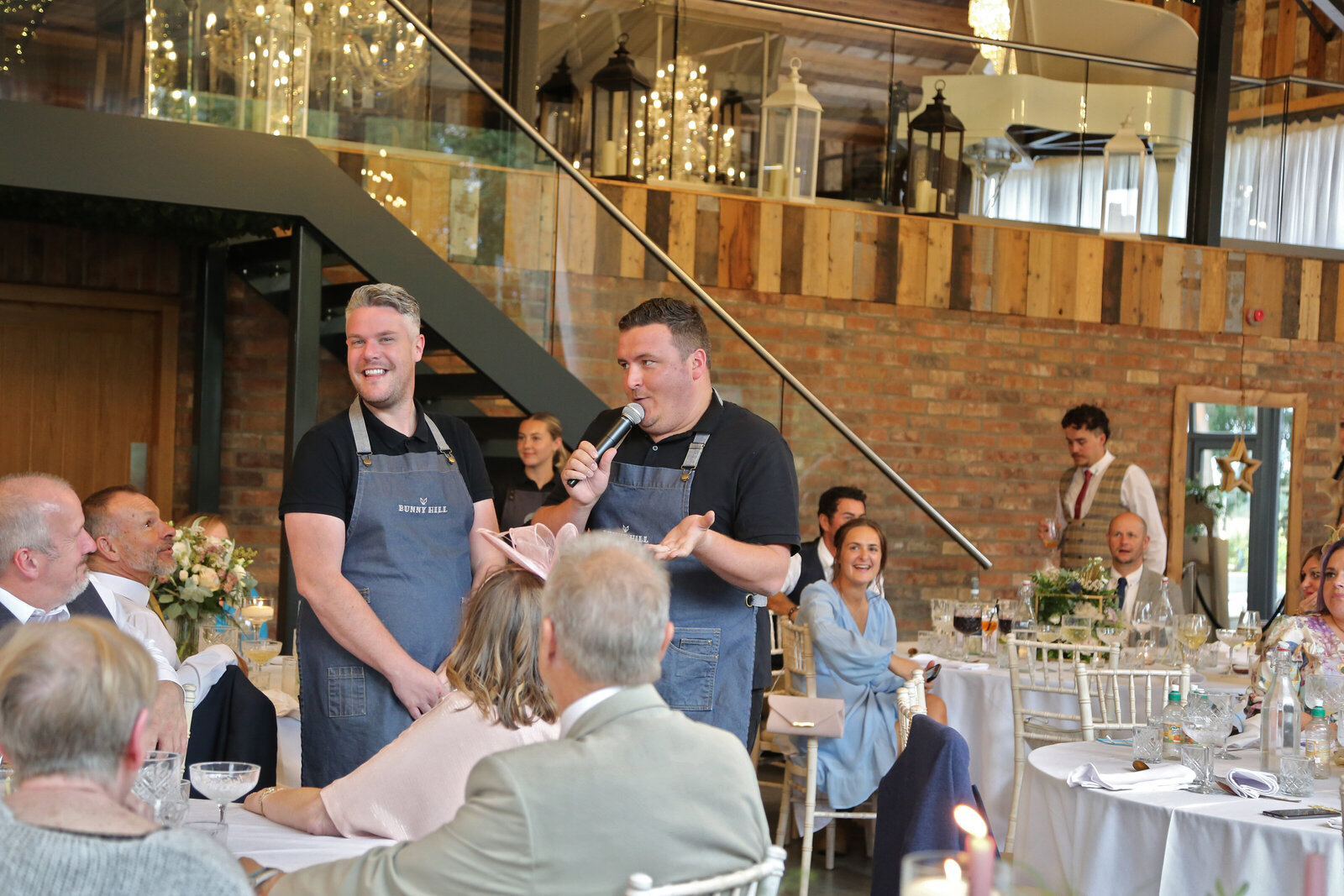 Two singing waiters in denim aprons performing at a wedding