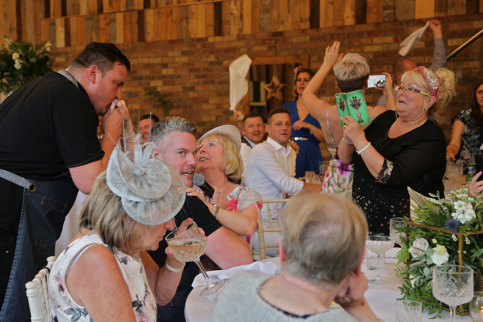 Wedding guests laughing and waving napkins at a barn wedding