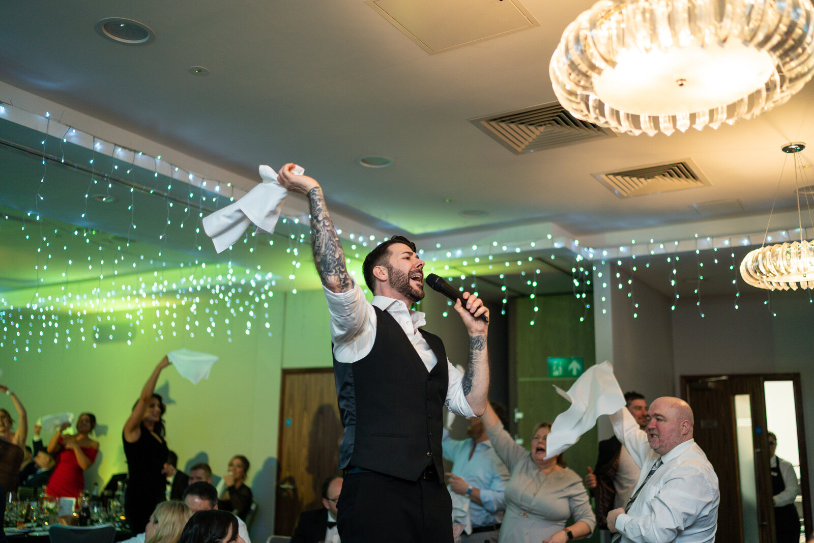 Singing waiter standing on a chair as guests wave napkins at a corporate event