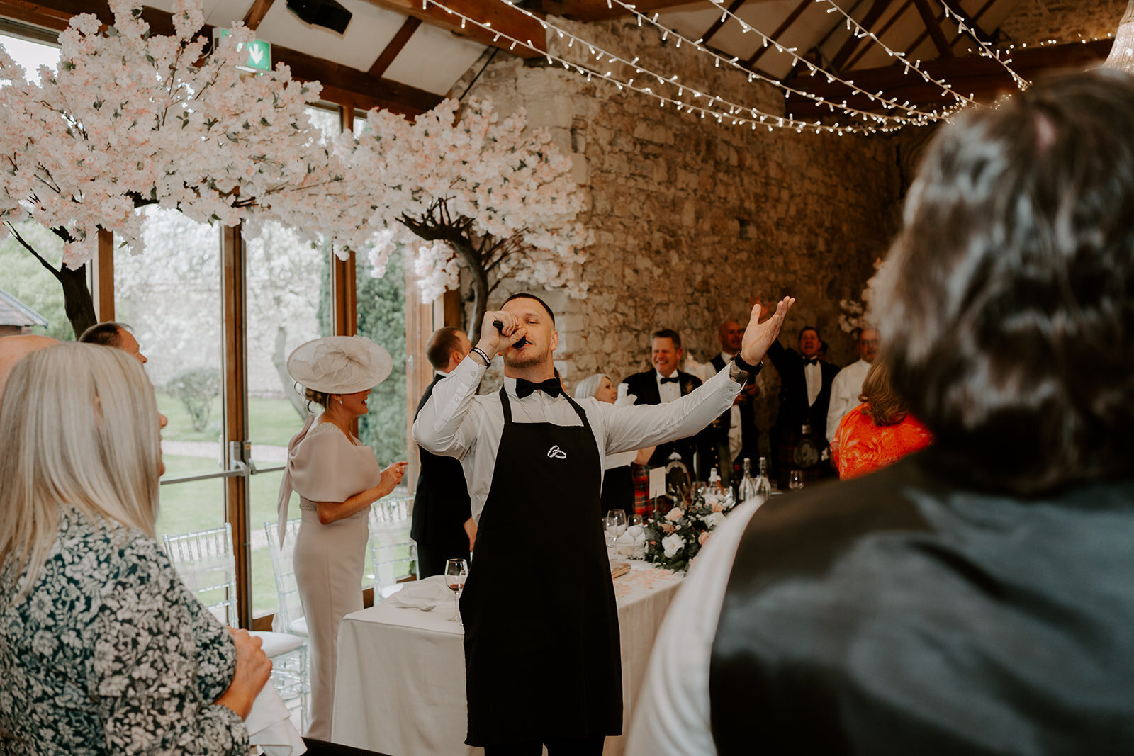Singing waiter performing in a rustic wedding venue with fairy lights