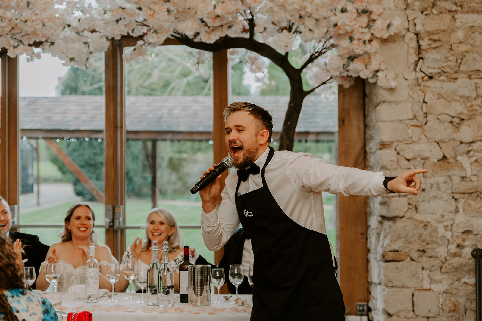 Singing waiter in an apron performing at a wedding with a floral backdrop