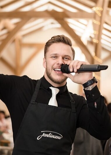 Singing waiter in a black apron performing in a timber-beamed venue
