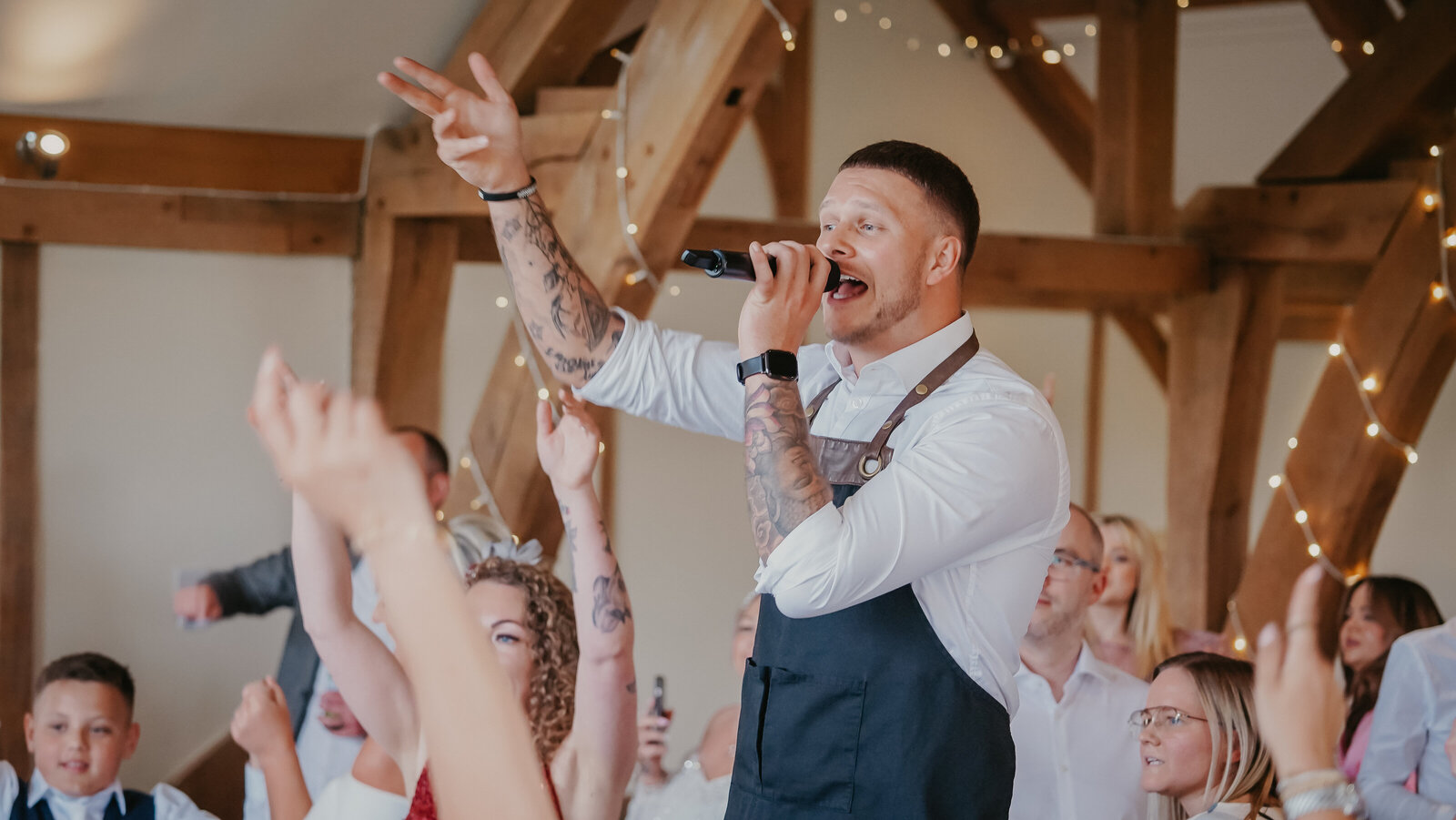 Singing waiter performing to guests with arms in the air at a barn wedding