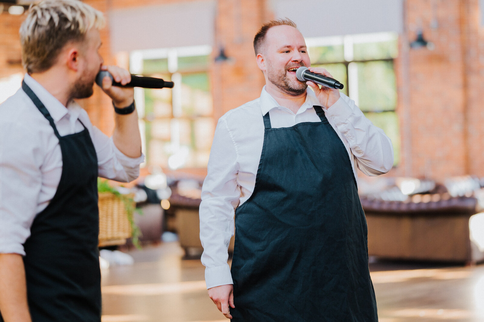 Two singing waiters in aprons performing with microphones at a wedding