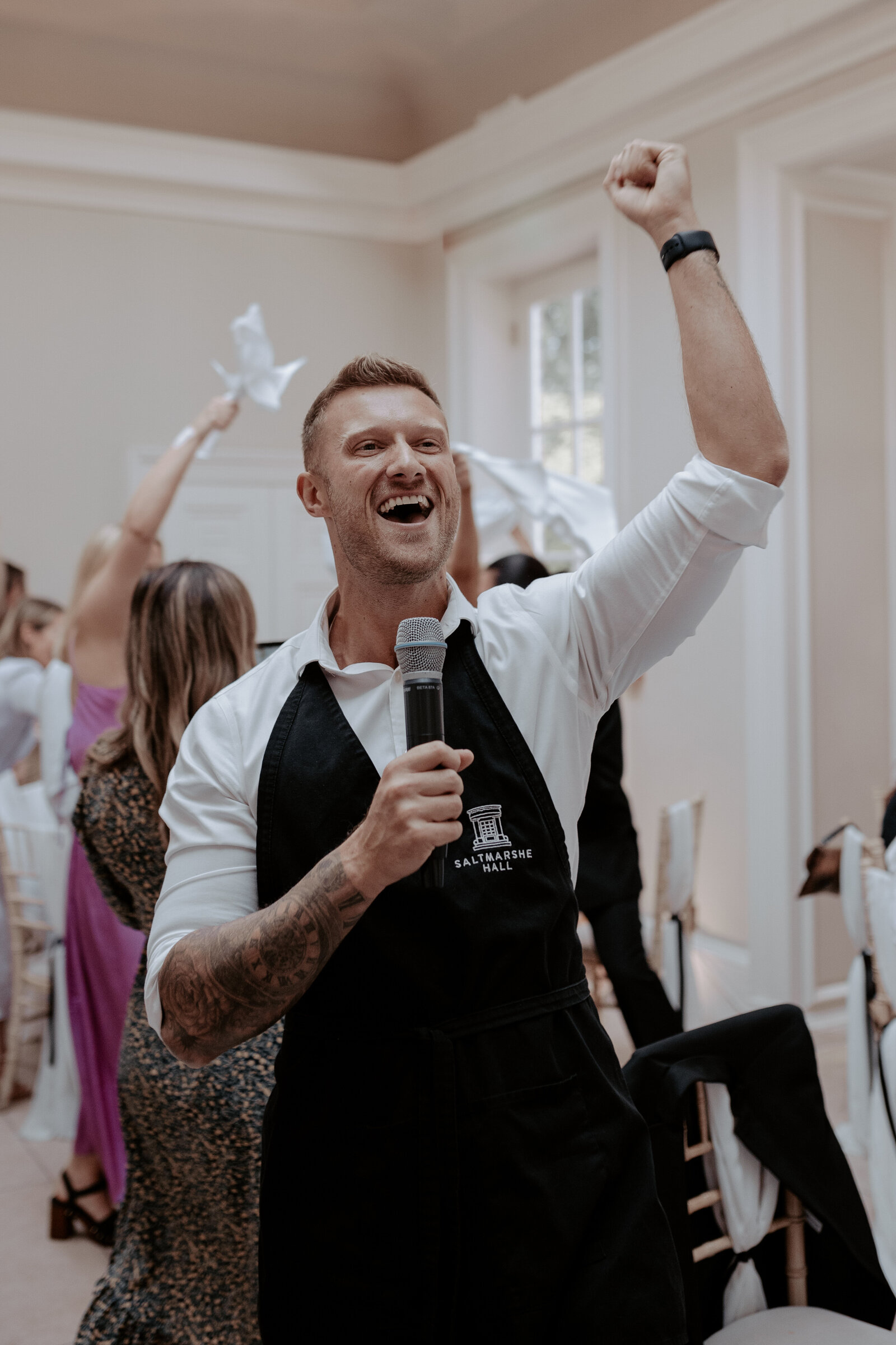 Singing waiter in an apron cheering with guests at a wedding